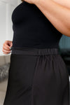 Side view of stitching on side of plus size model wearing poly satin black maxi skirt with full coverage