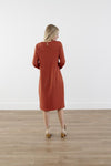 Back of rich-toned modest knit dress with long puff sleeves, straight silhouette, and knee-length hem, made from cozy polyester-rayon-spandex blend