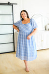 Plus size model wearing modest blue plaid midi dress with puff sleeves and smocked bodice shown from the front
